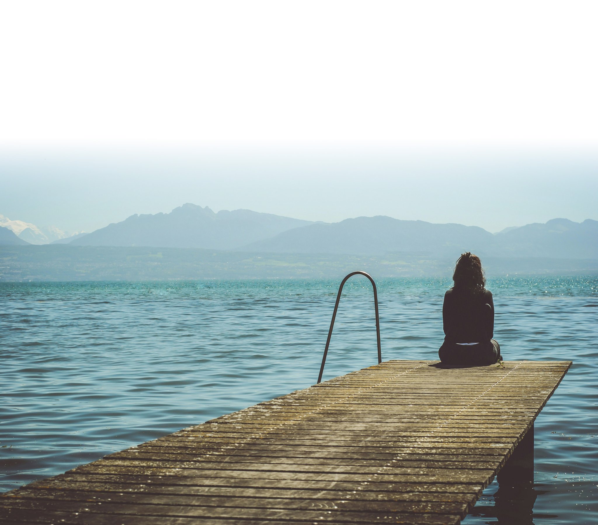 A woman sitting on a dock looking out at a body of water